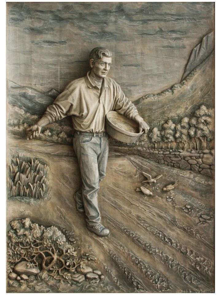 A relief in lime: a man in an open shirt walks across a ploughed field casting seed from his bag, with birds on the ground and mountains behind.
